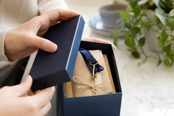 Hands lift the lid of a navy box revealing envelopes tied with twine and a brass key