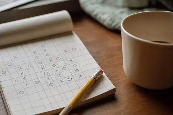 A hand-drawn deduction grid of crosses and circles on a notepad with a pencil