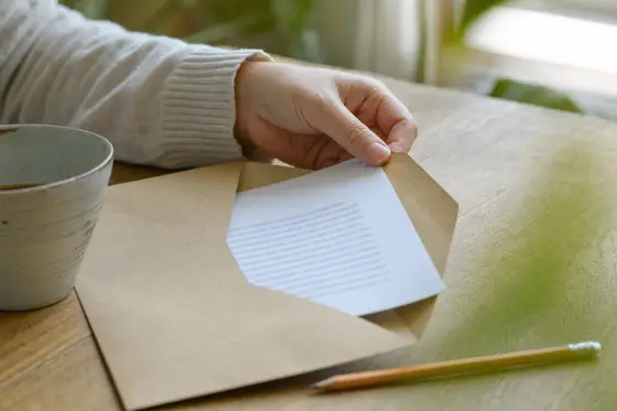 A hand slides the first document out of a kraft envelope on a kitchen table